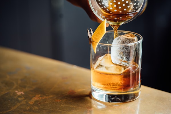 Location A cocktail being poured into a glass over a large ice cube