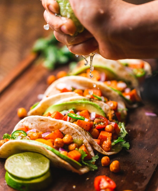 Location A row of tacos with a hand squeezing lime over them