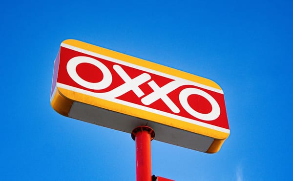 Location OXXO convenience store sign against a clear blue sky, with an “abierto 24 horas” panel under it