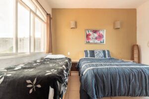 Spaces Bedroom with two beds against a yellow wall and a window across the full width