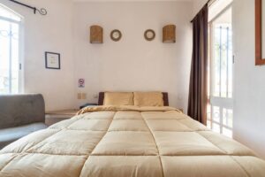 Spaces Bedroom with a beige bed, woven wall discs and a sofa beside the window