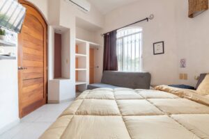Spaces Bedroom with a tall arched wooden door, a sofa under the window and a beige bed