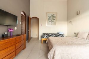 Spaces Bedroom with a wall-mounted TV, a wooden dresser and a bench at the foot of the bed