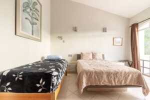 Spaces Bedroom with two beds under a high ceiling, a framed botanical print and a curtain